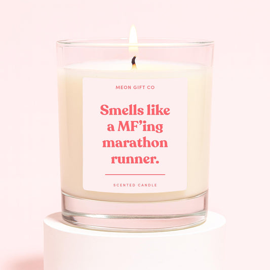 Lit scented candle in clear glass jar, cream wax, label “Smells like a MF'ing marathon runner”