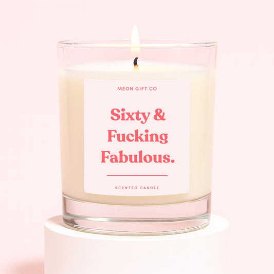Glass jar scented candle with flame; cream label reading "Sixty & Fucking Fabulous"