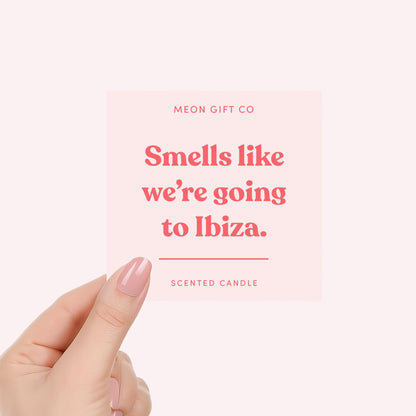 Scented candle label close-up held by hand, pink text on pale background